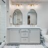 Stylish bathroom with glass shower, double vanity, gold fixtures, and patterned floor tiles.
