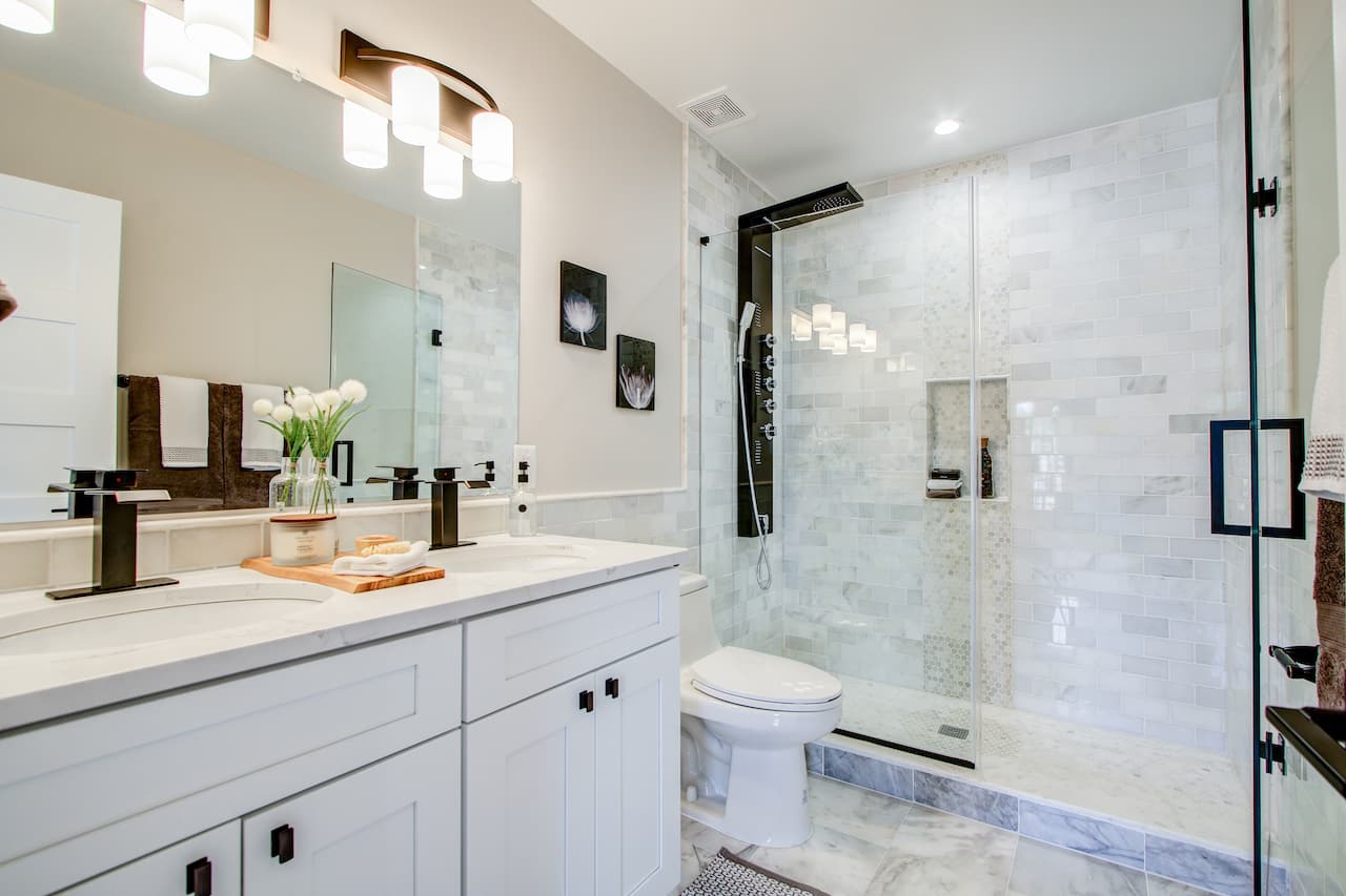 Modern bathroom featuring a double vanity, large mirror, and glass shower enclosure