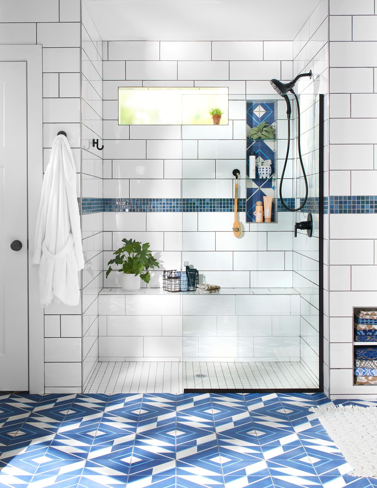 Bright bathroom with sliding glass shower, white subway tiles, blue accent tiles, and patterned blue floor.