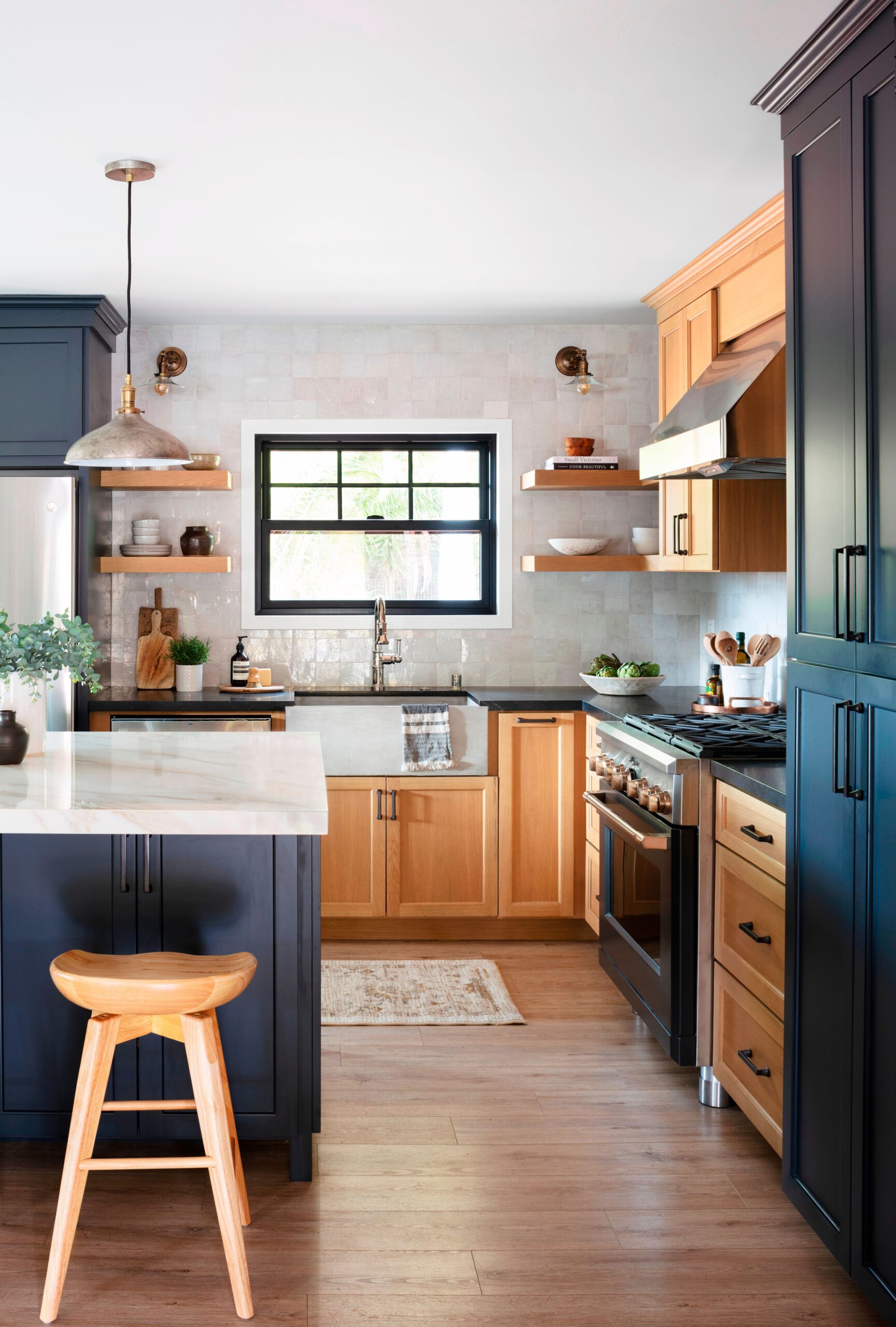 Warm farmhouse kitchen featuring two-tone cabinetry with navy blue and natural wood cabinets, open shelves, and a marble island countertop.