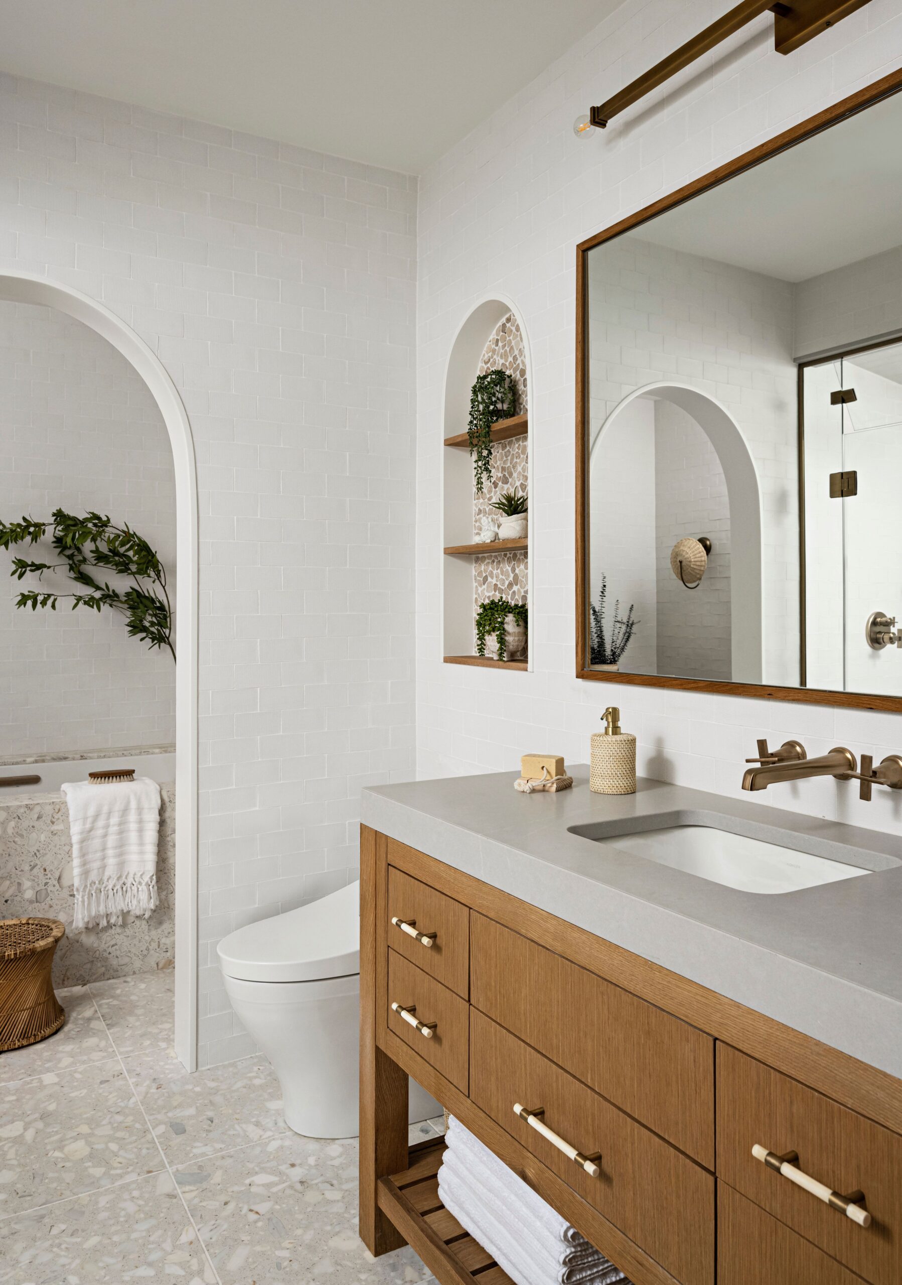Modern bathroom with wood vanity, large mirror, and arched wall niches