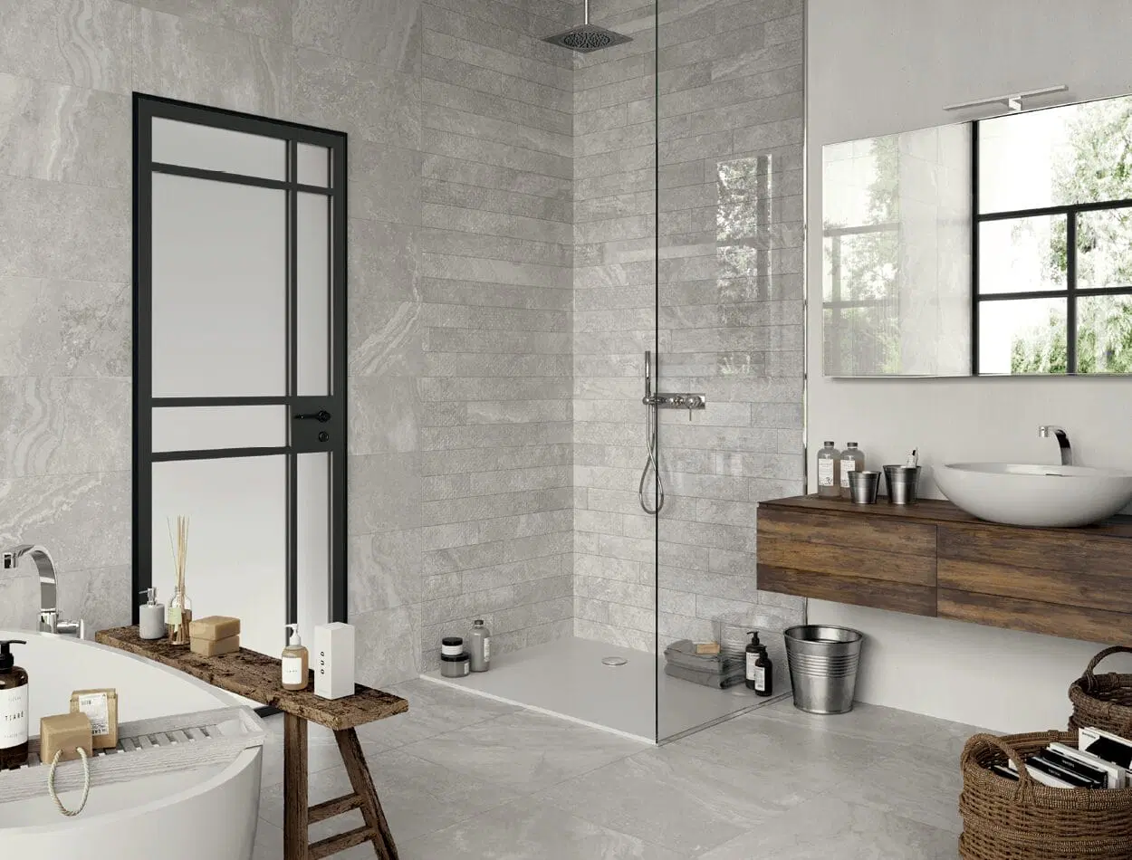 Contemporary bathroom featuring gray stone tiles, a frameless glass walk-in shower, a floating wooden vanity with a vessel sink, and black-framed windows.