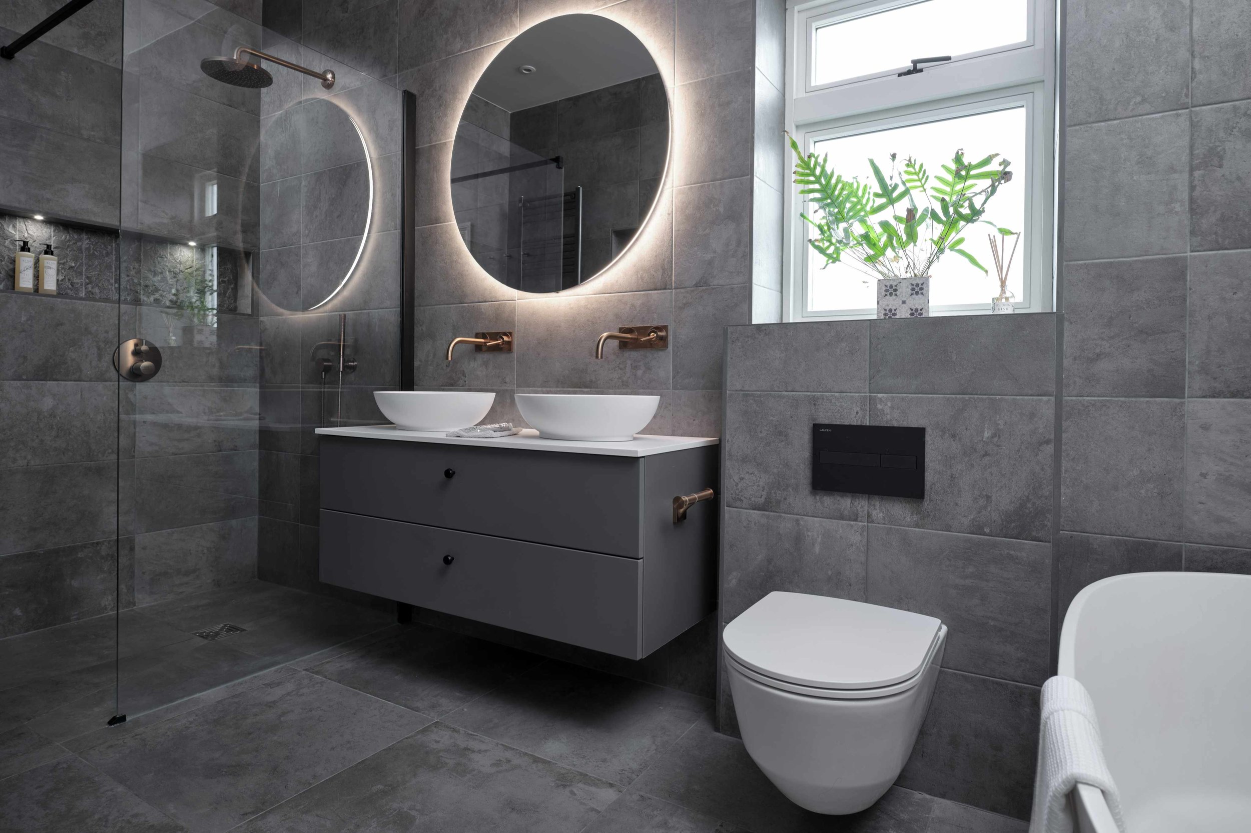 Contemporary bathroom featuring grey large-format tiles, a floating vanity with vessel sinks, round LED mirrors, and a glass walk-in shower.