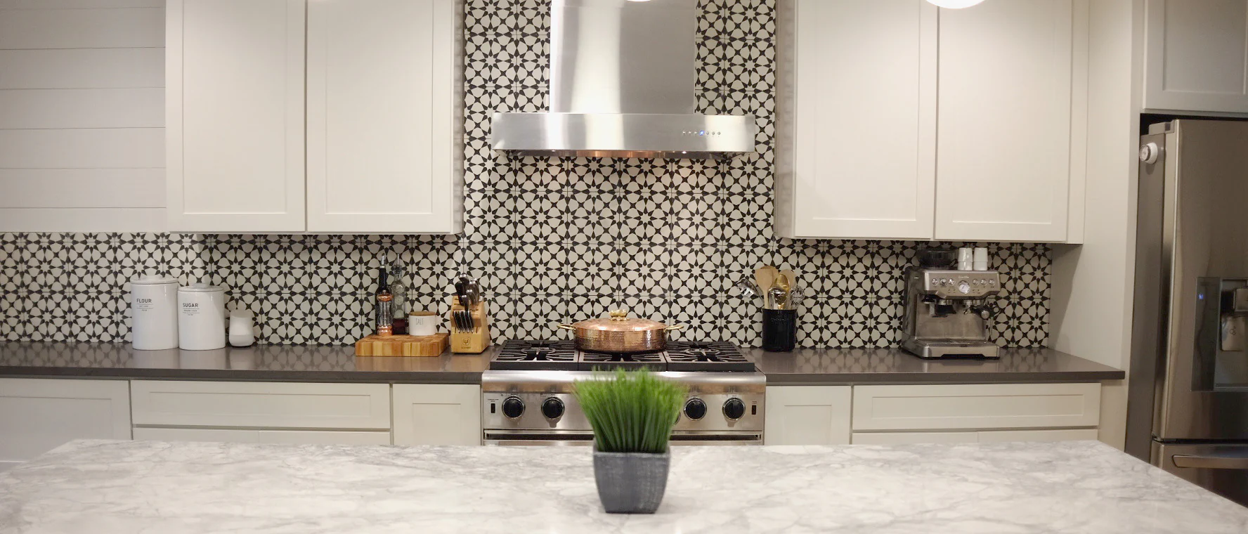 Stylish kitchen featuring white cabinets, a patterned black and white tile backsplash, stainless steel appliances, and a marble island countertop.
