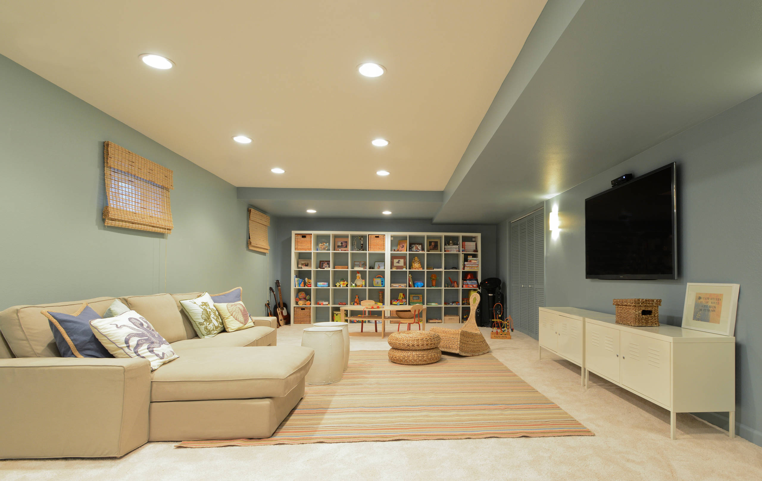 A basement designed for family use featuring a cozy sectional, kids’ play zone, and a large shelving unit.