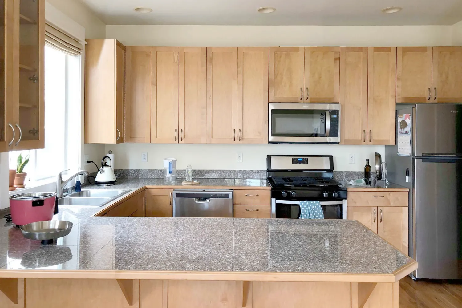 Kitchen featuring light wood cabinetry, granite countertops, stainless steel appliances, and a spacious island under bright natural light.