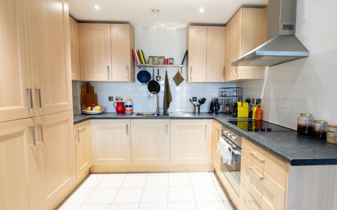 Compact modular kitchen with light wood cabinets, black countertops, and white tiled backsplash, optimized for small spaces.