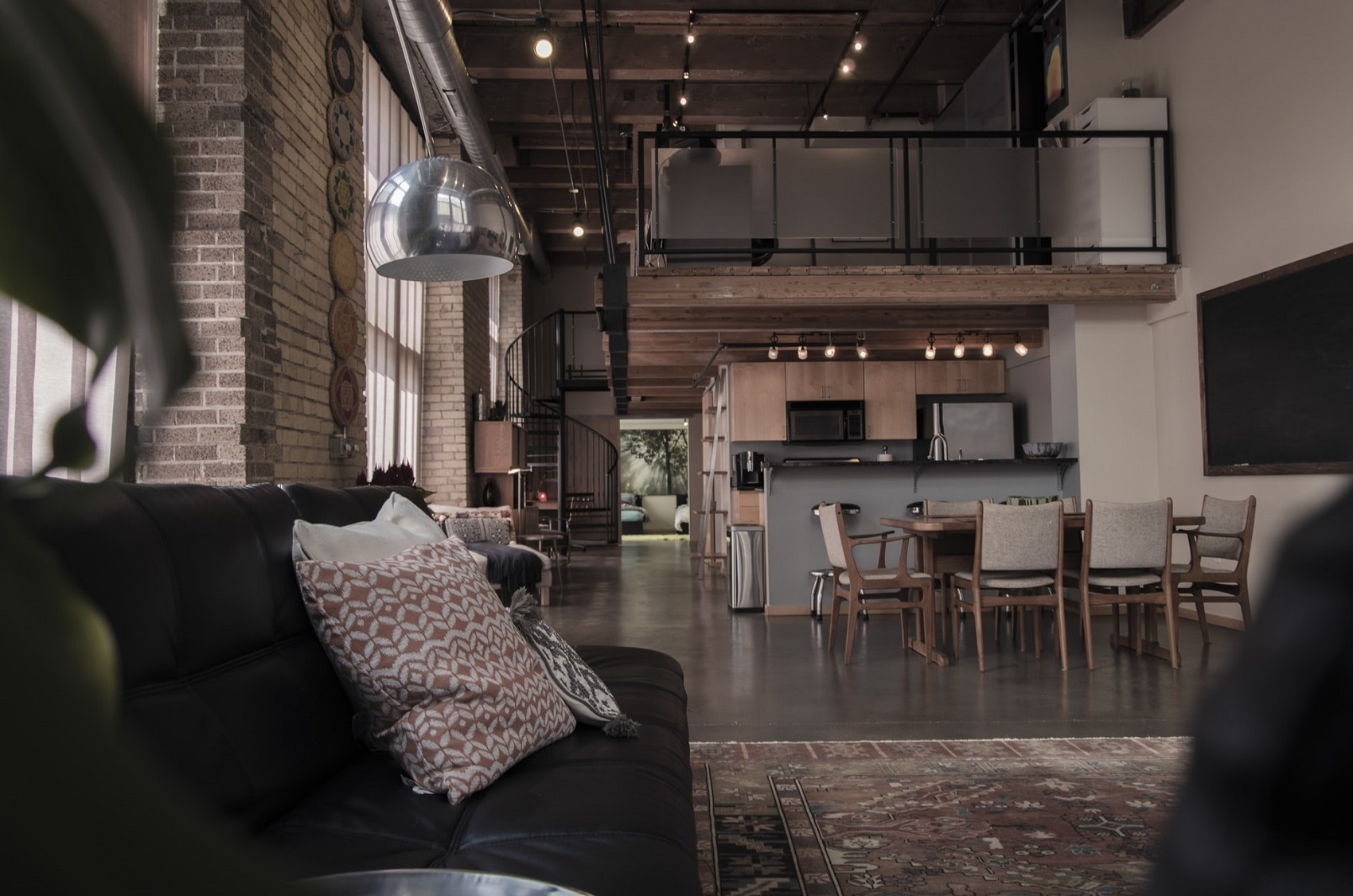 Spacious loft featuring exposed brick walls, wooden ceiling beams, a modern kitchen with dining area, and a cozy living space with patterned pillows.