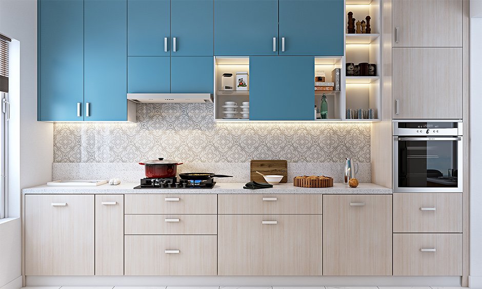 Contemporary kitchen featuring upper blue cabinets, lower light wood cabinetry, built-in oven, patterned backsplash, and under-cabinet lighting.