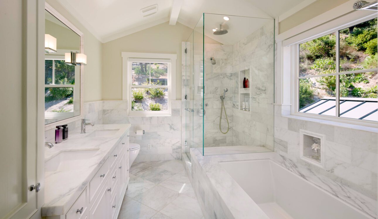 Bright bathroom with marble walls, glass shower, and built-in bathtub.