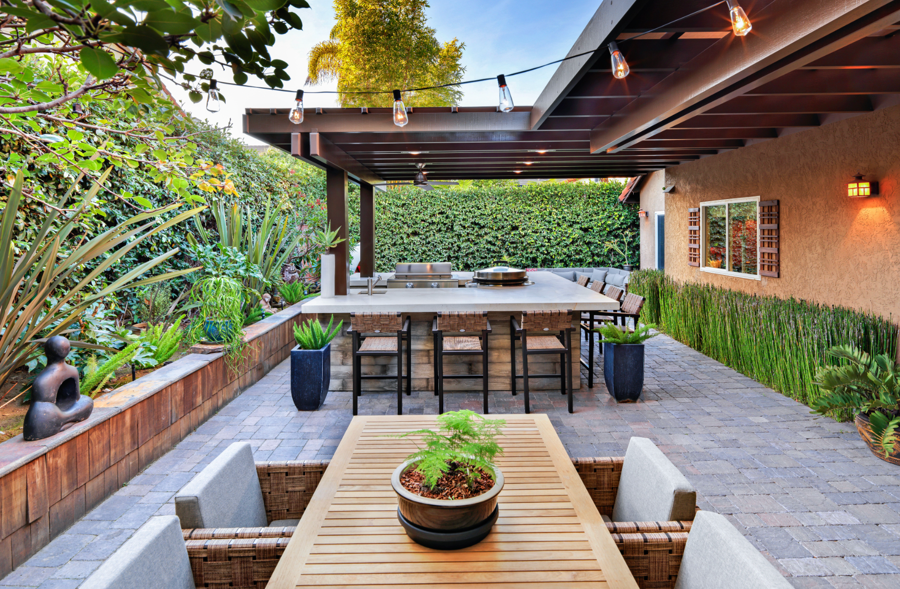 Outdoor patio with covered kitchen, dining area, and lush greenery.