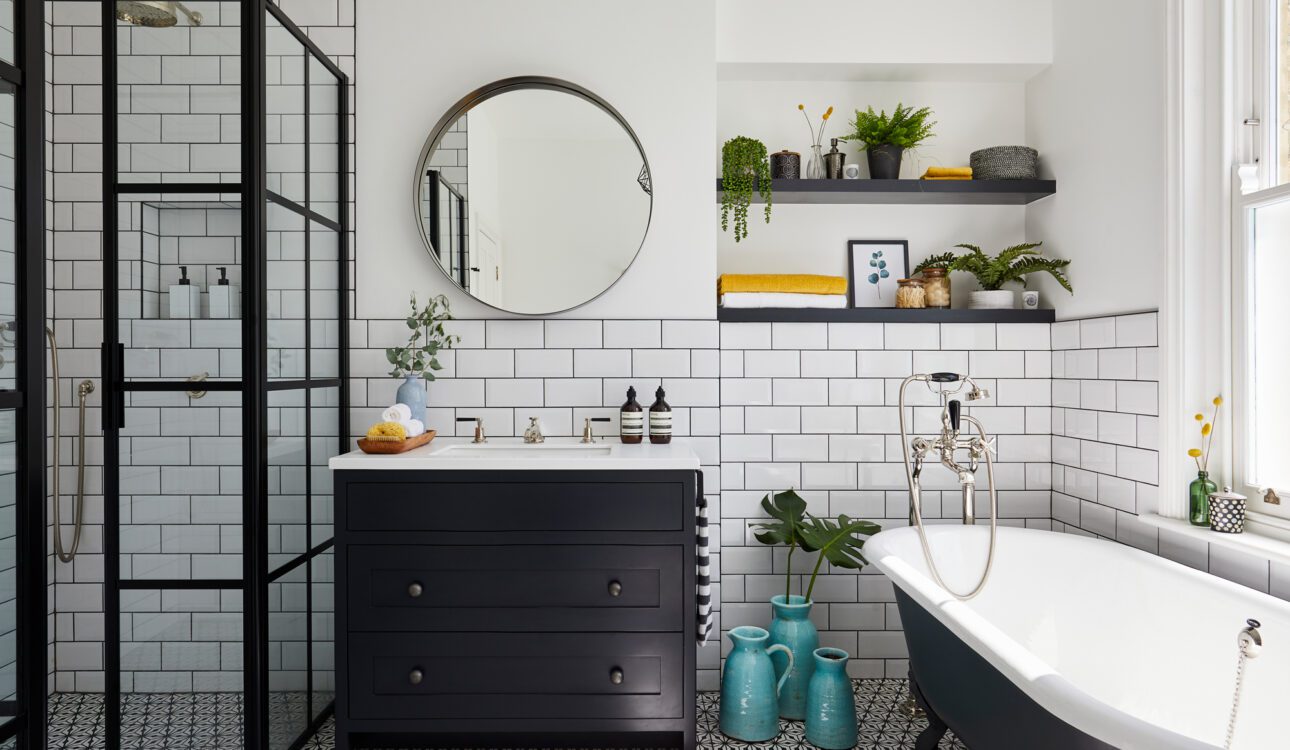 Modern bathroom featuring white subway tiles, a black framed glass shower, a dark vanity with a round mirror, patterned floor tiles, and a clawfoot bathtub.