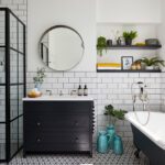 Modern bathroom featuring white subway tiles, a black framed glass shower, a dark vanity with a round mirror, patterned floor tiles, and a clawfoot bathtub.