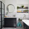 Modern bathroom featuring white subway tiles, a black framed glass shower, a dark vanity with a round mirror, patterned floor tiles, and a clawfoot bathtub.