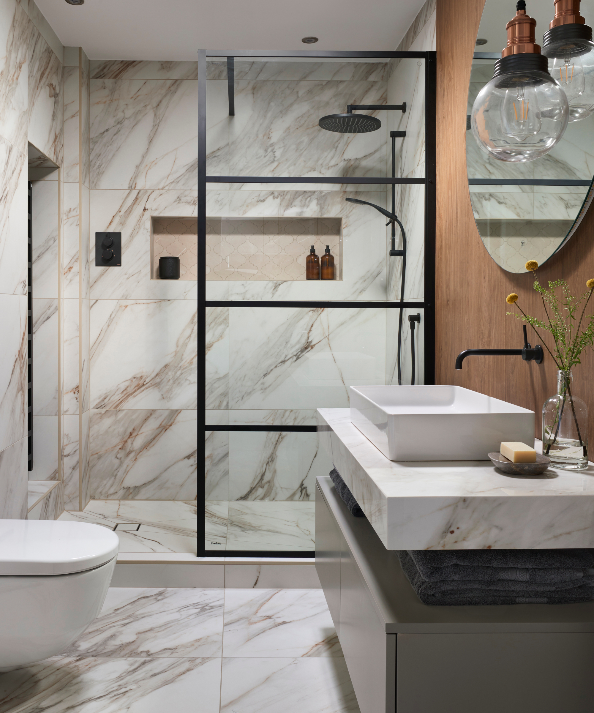 Luxurious bathroom featuring marble walls and floors, a black-framed glass shower enclosure, vessel sink on a marble countertop, and matte black fixtures.