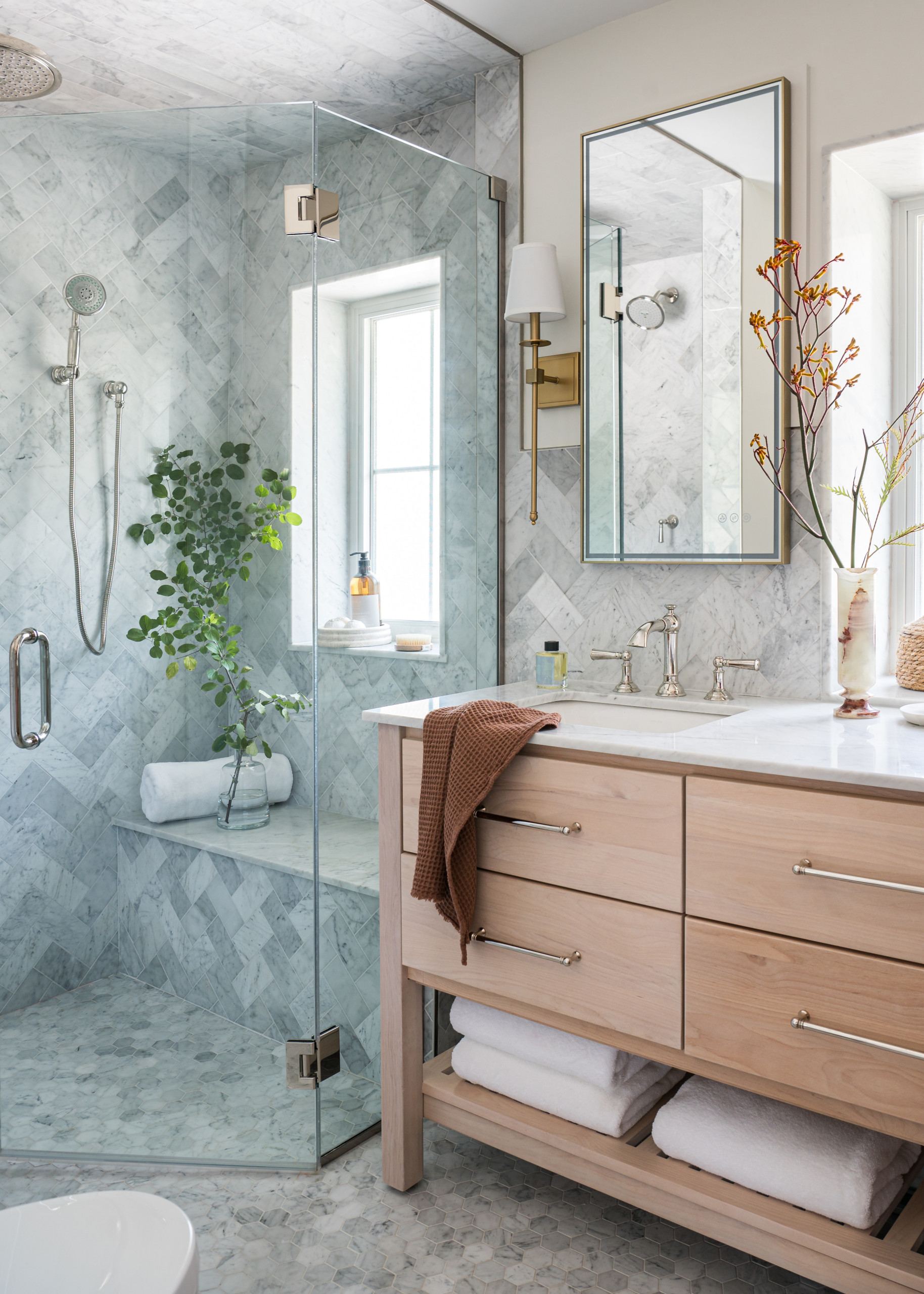 Small modern bathroom with glass shower, light wood vanity, and marble tiles.