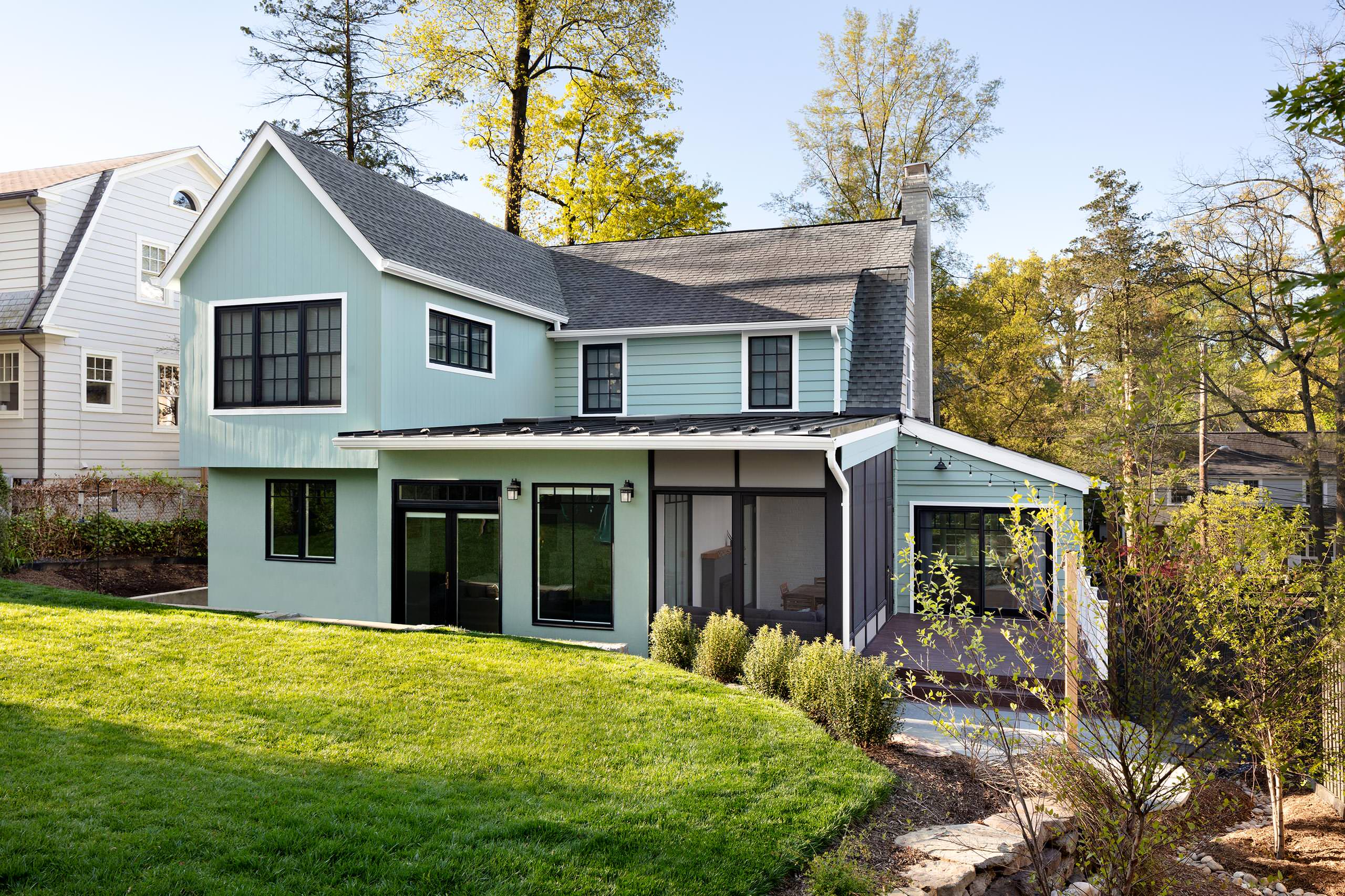 Modern suburban home with light green siding, black-trimmed windows, and landscaped backyard.
