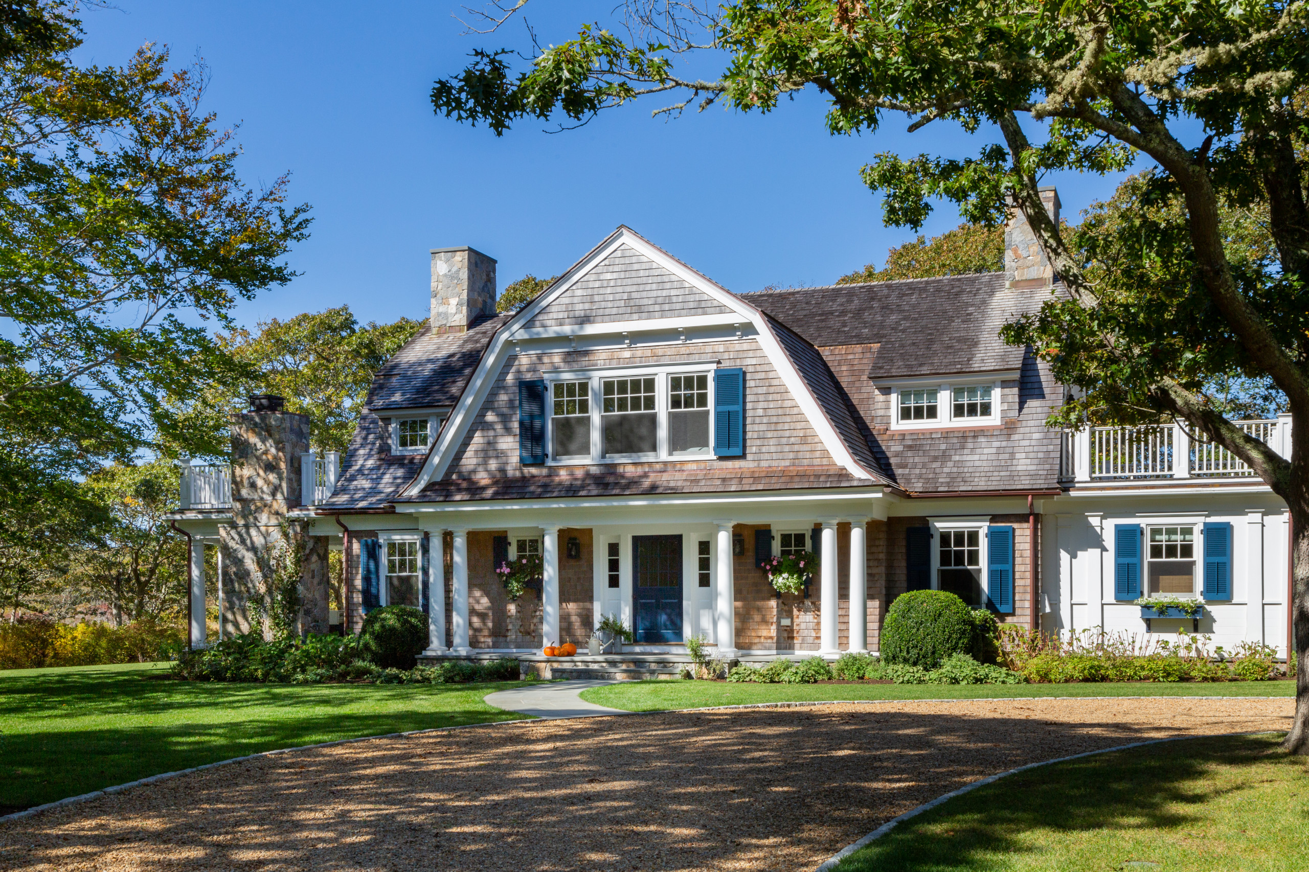 Traditional two-story home with blue shutters, stone chimneys, and front porch columns.