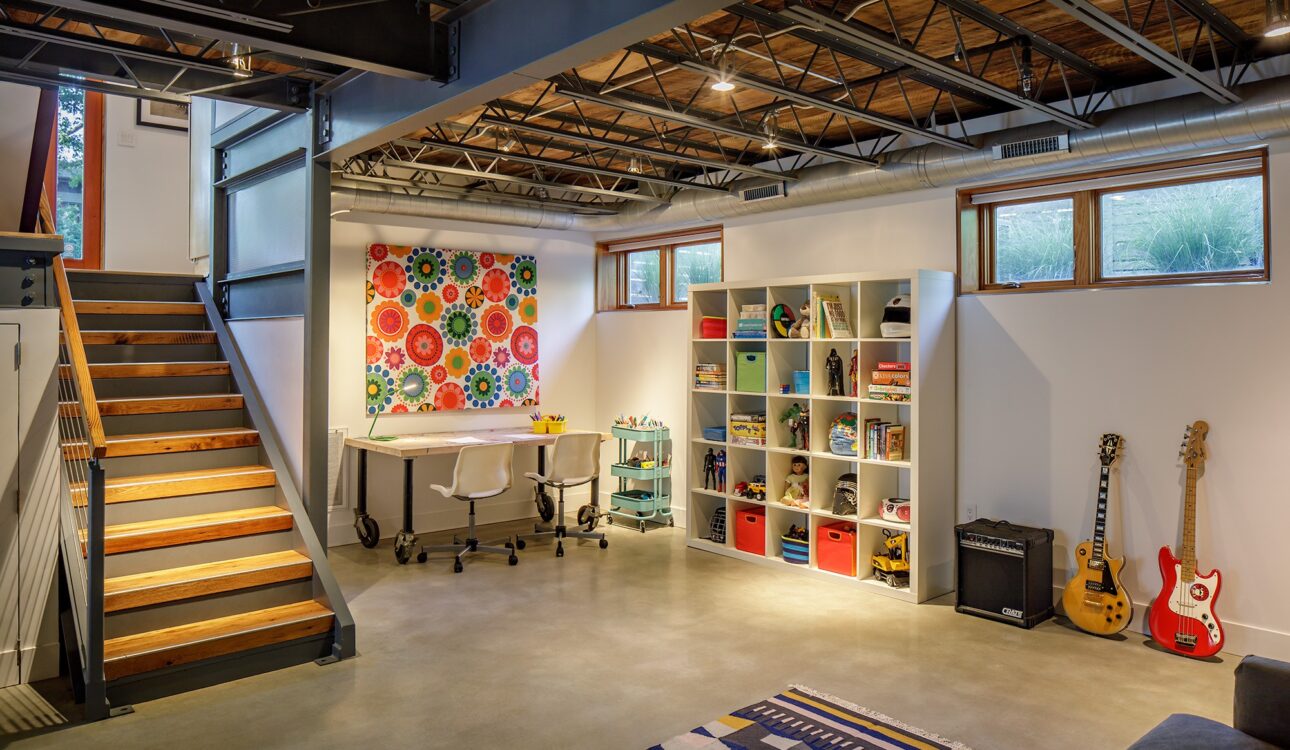Modern basement with open ceiling beams, colorful art, and kids’ play area.