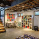 Modern basement with open ceiling beams, colorful art, and kids’ play area.