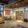 Modern basement with open ceiling beams, colorful art, and kids’ play area.
