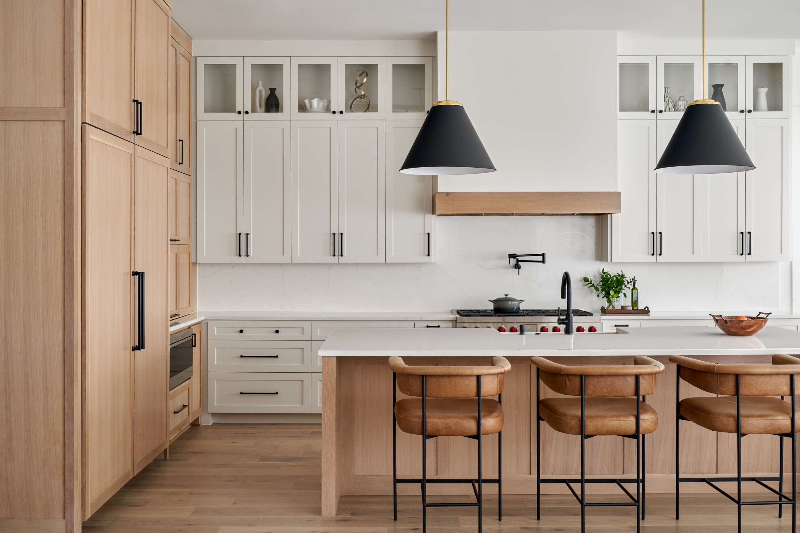 Modern kitchen with natural wood cabinets, white countertops, and leather bar stools