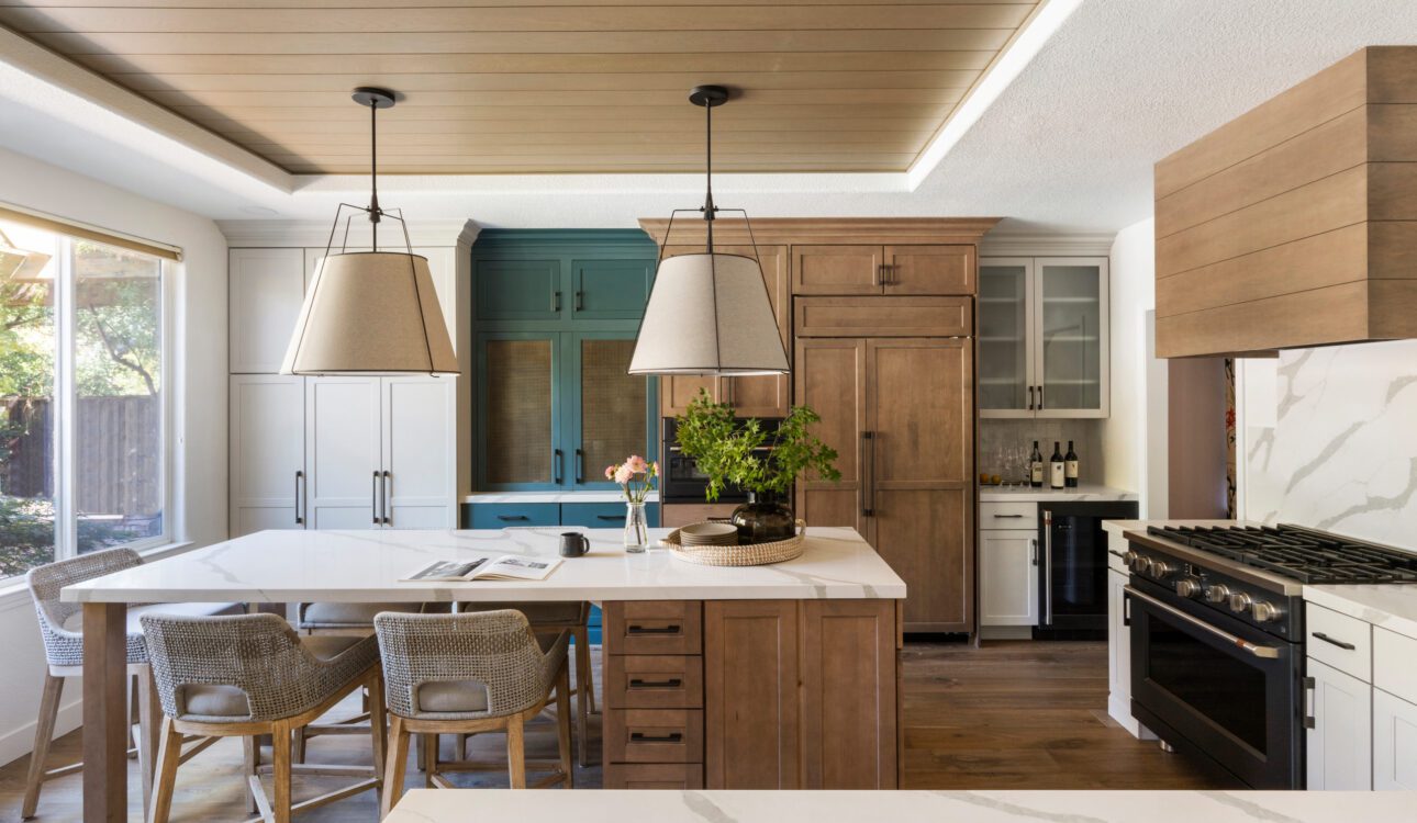 Contemporary kitchen with wood accents, a central island, and mixed cabinet finishes including teal, white, and natural wood tones.