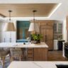 Contemporary kitchen with wood accents, a central island, and mixed cabinet finishes including teal, white, and natural wood tones.