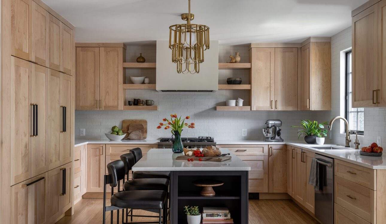 Warm wood kitchen with shaker cabinets, open shelves, black island seating, and brass chandelier