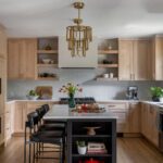 Warm wood kitchen with shaker cabinets, open shelves, black island seating, and brass chandelier