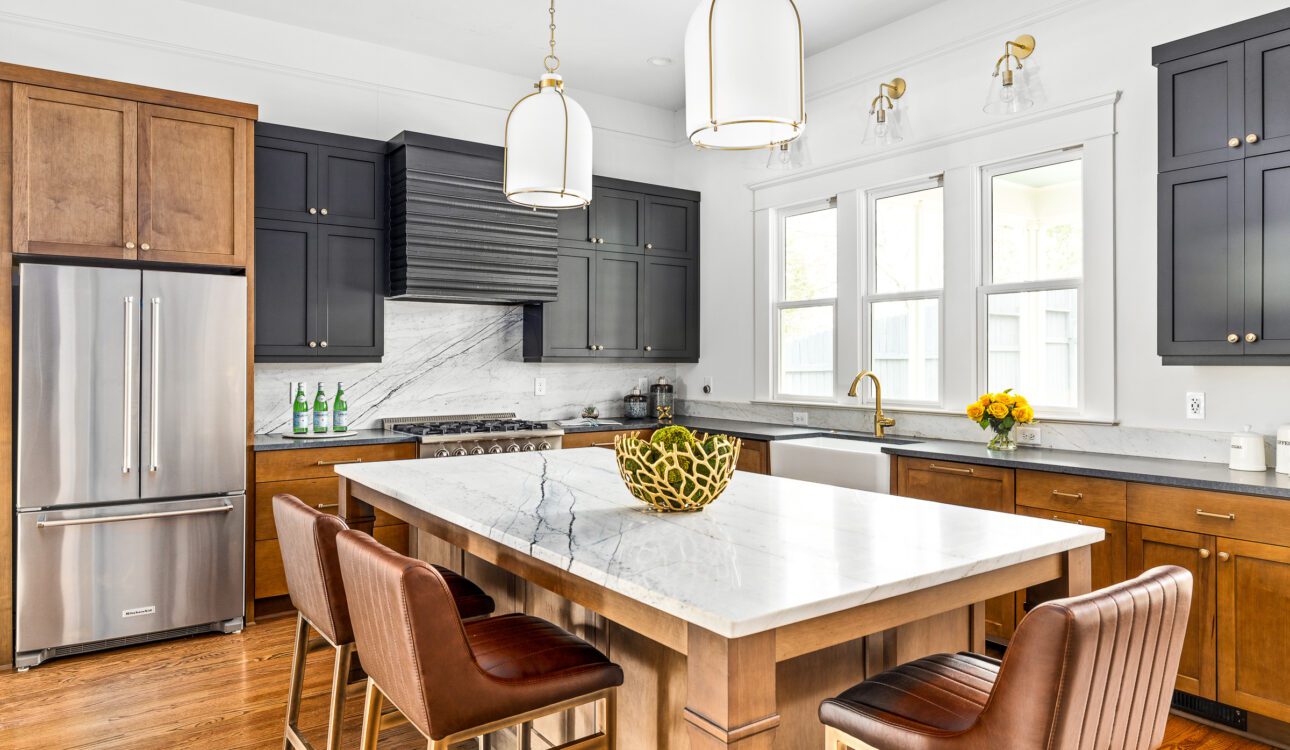 Transitional kitchen with black and wood cabinets, marble island, gold fixtures, and leather barstools