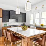 Transitional kitchen with black and wood cabinets, marble island, gold fixtures, and leather barstools