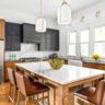Transitional kitchen with black and wood cabinets, marble island, gold fixtures, and leather barstools