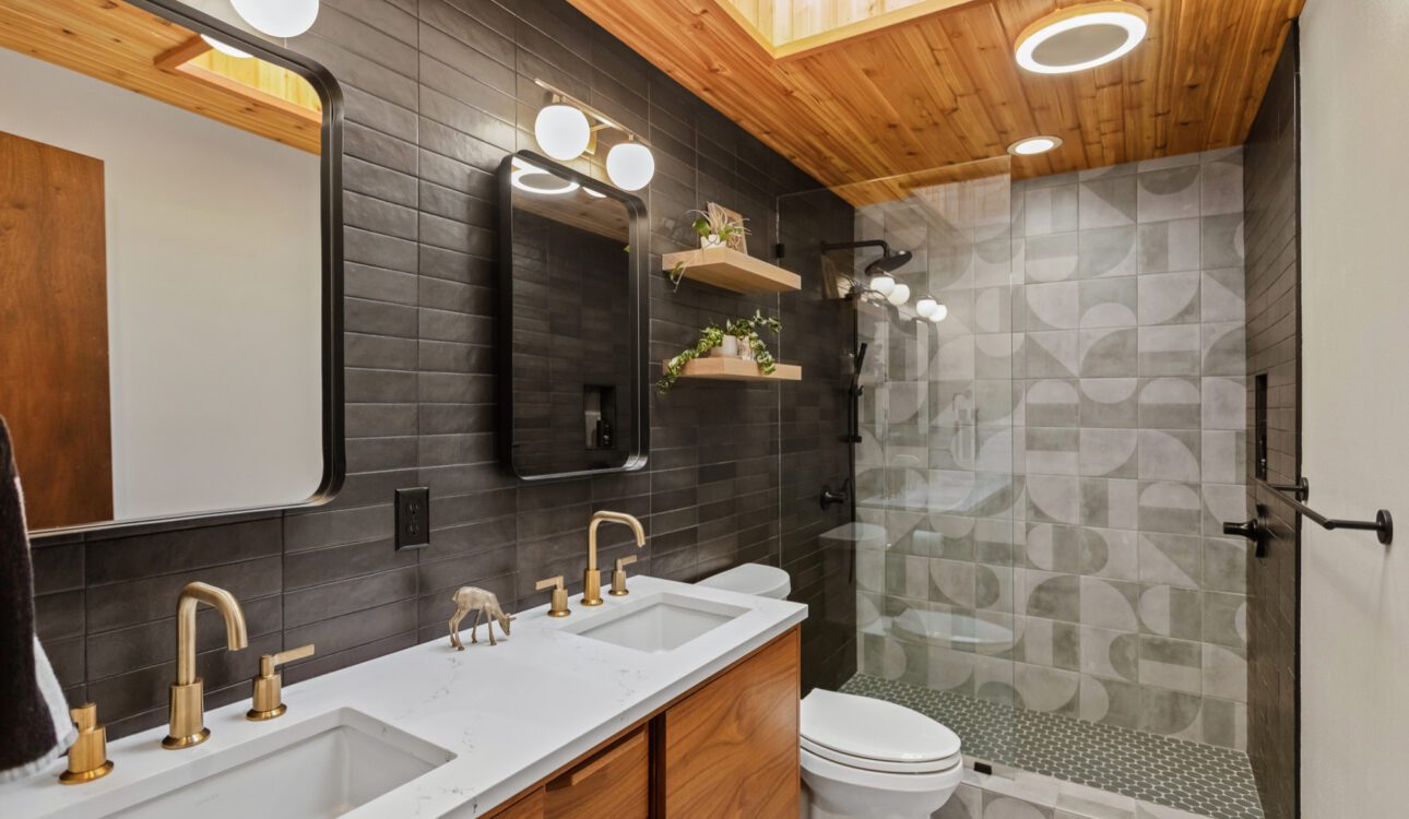 Modern bathroom with double vanity, matte black tile, wood ceiling, and geometric shower design