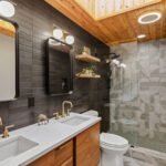 Modern bathroom with double vanity, matte black tile, wood ceiling, and geometric shower design