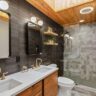 Modern bathroom with double vanity, matte black tile, wood ceiling, and geometric shower design