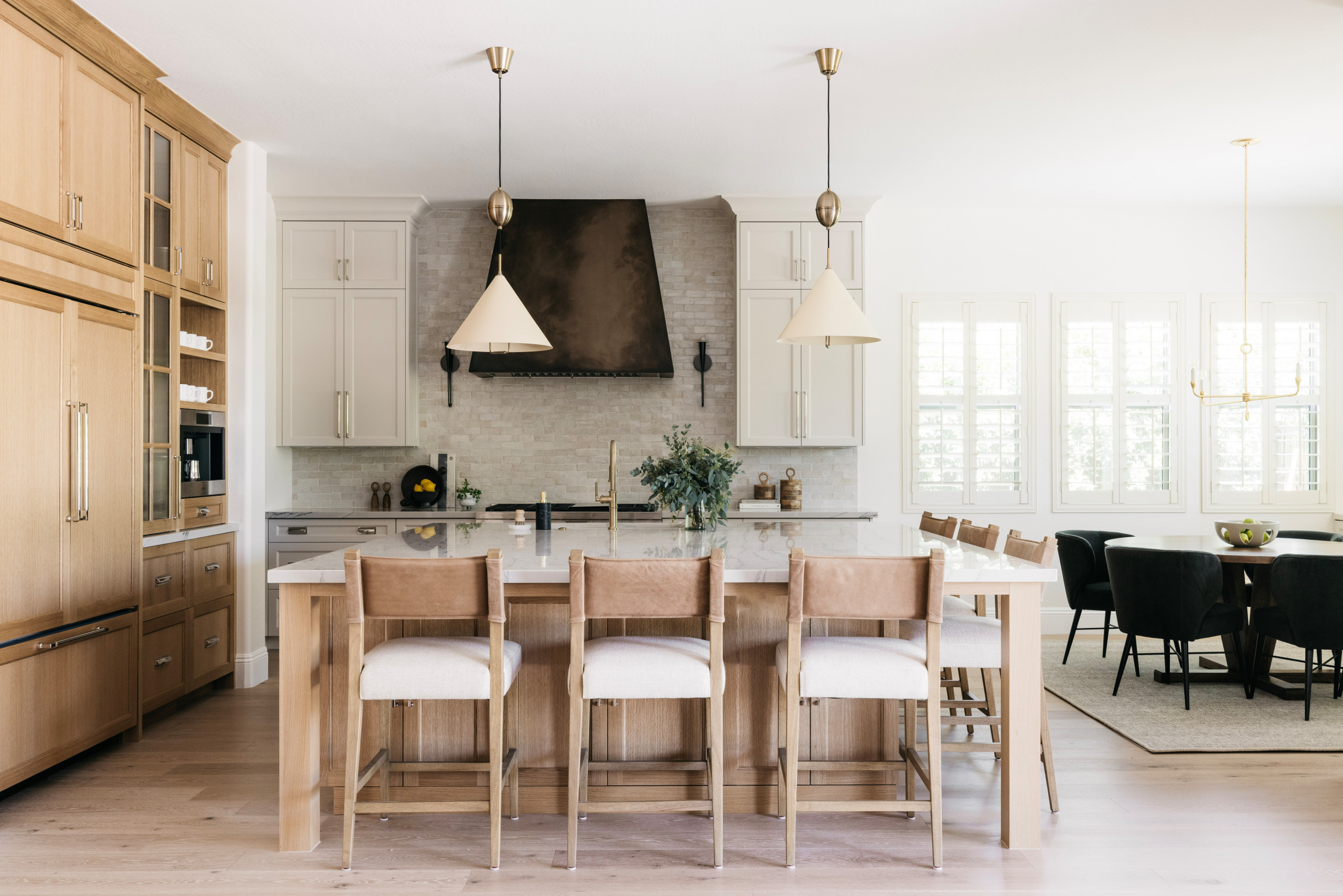 Spacious kitchen with light wood cabinetry, marble island, leather barstools, and open dining area