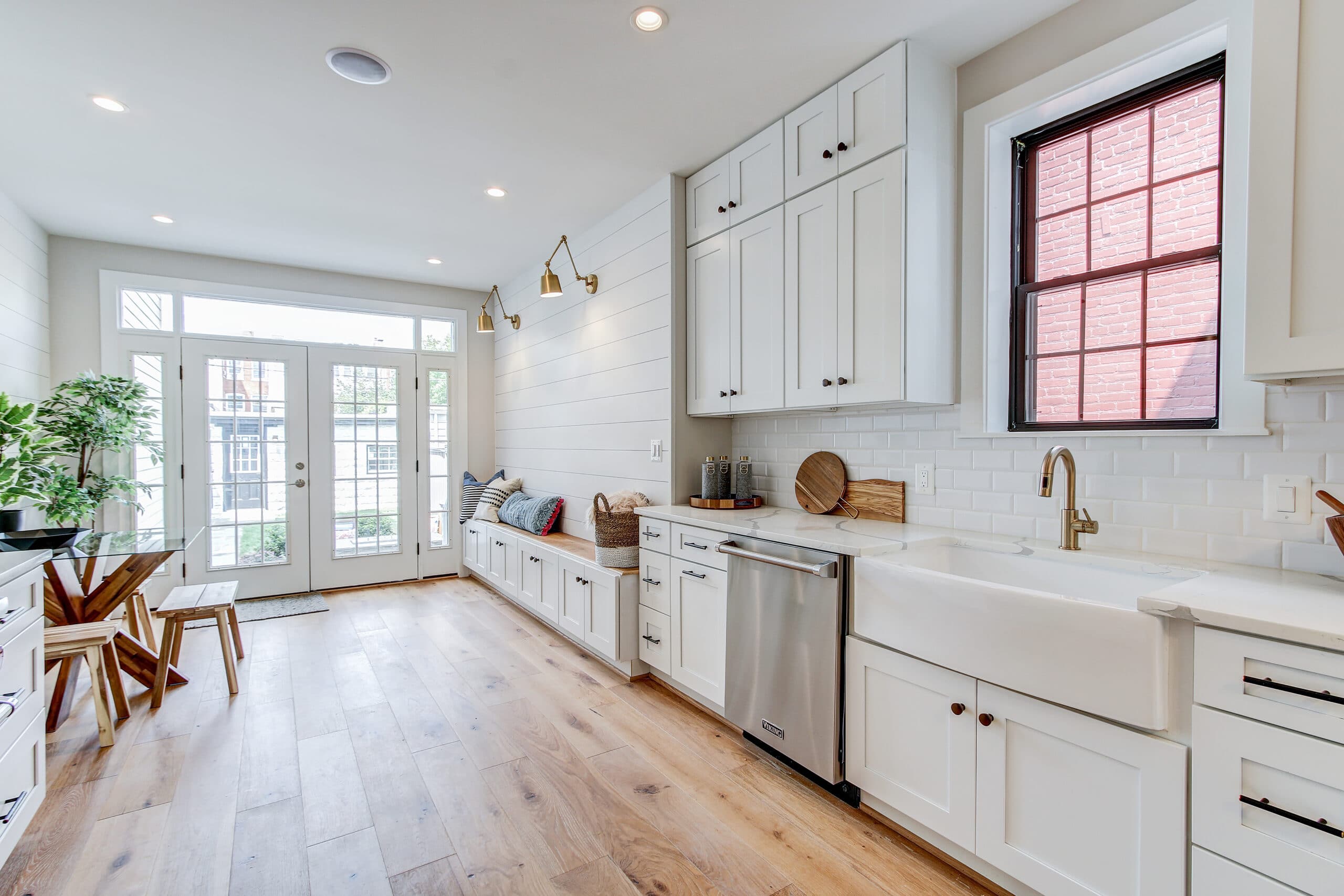 Bright white farmhouse-style kitchen with natural wood floors and built-in bench seating.