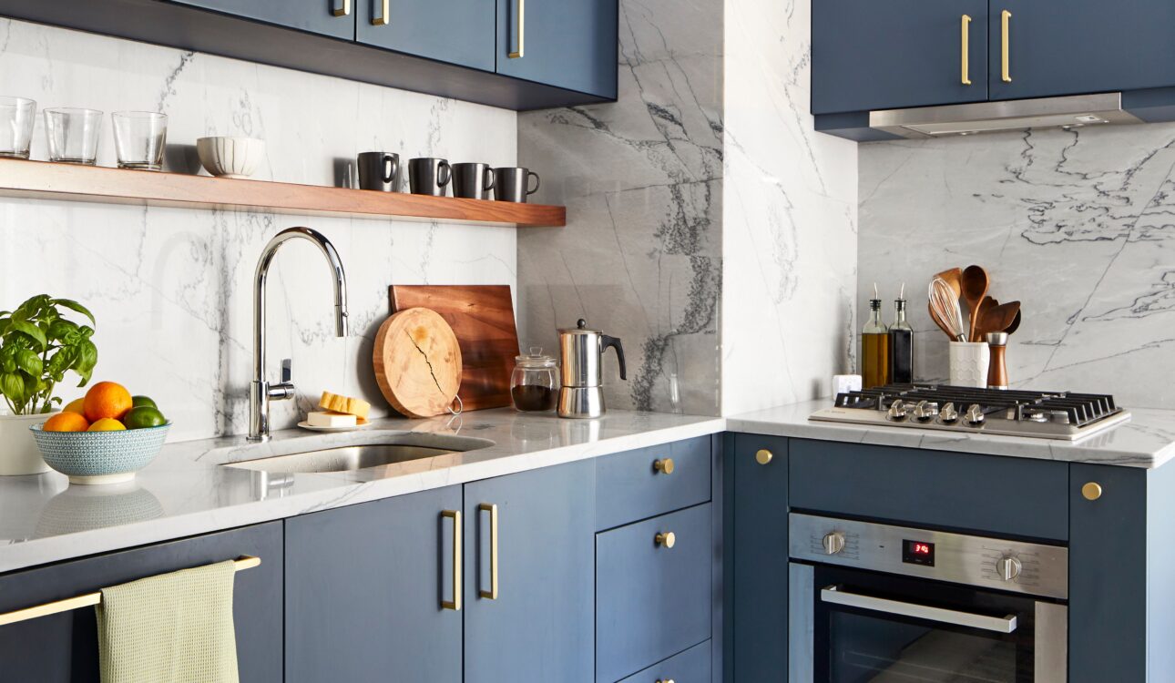 Contemporary kitchen with navy blue cabinets, marble backsplash, and gold hardware