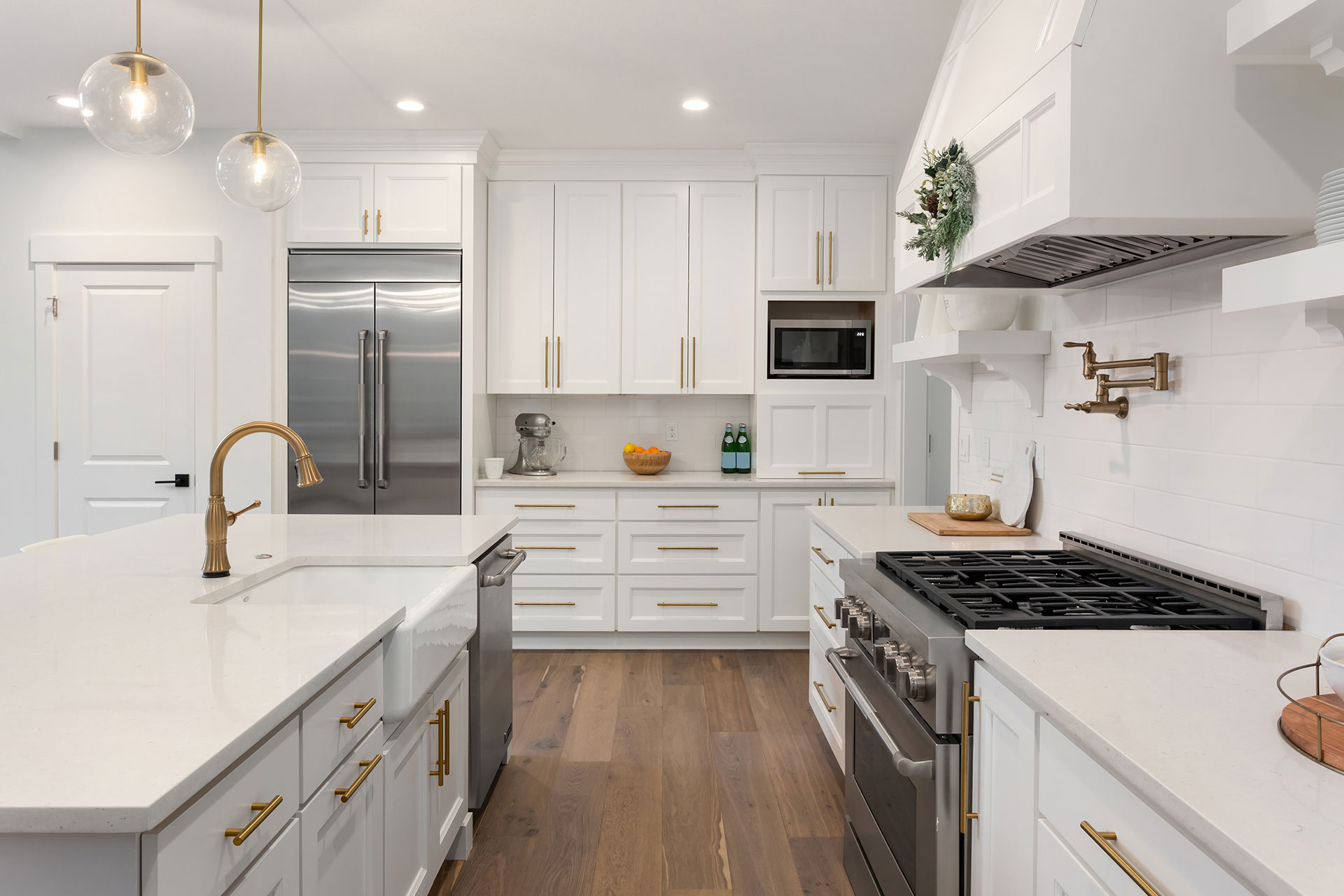 Modern white kitchen with brass hardware, stainless steel appliances, and wood flooring
