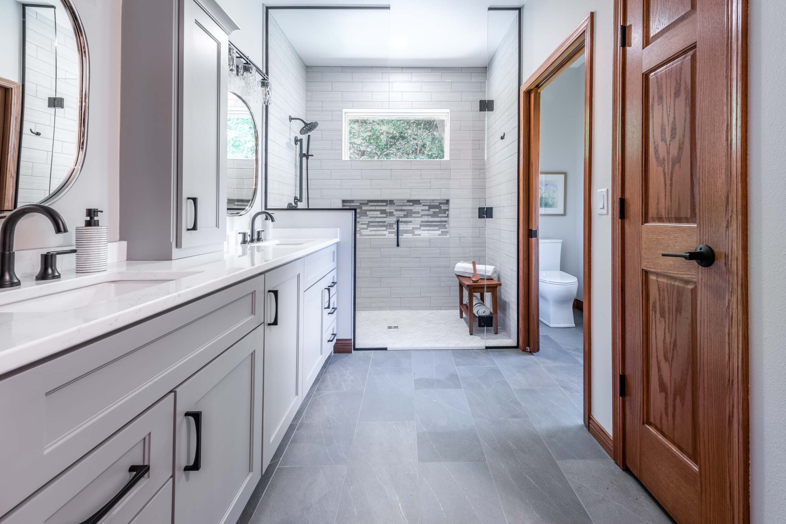 Modern bathroom with double vanity, walk-in shower, gray tile floors, and wood accents.