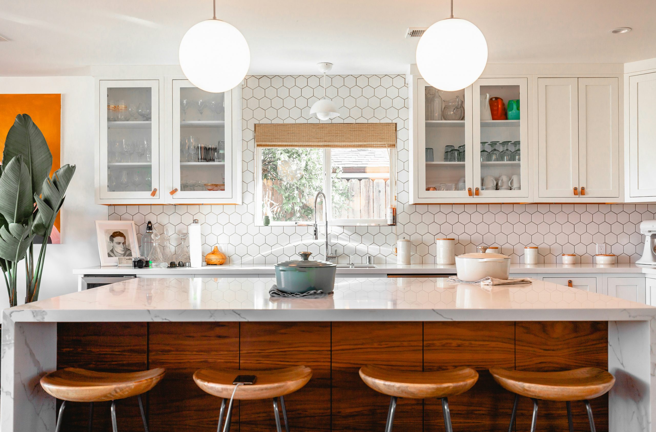 Modern kitchen with white hex tile backsplash, marble island, wood stools, and glass-front cabinets