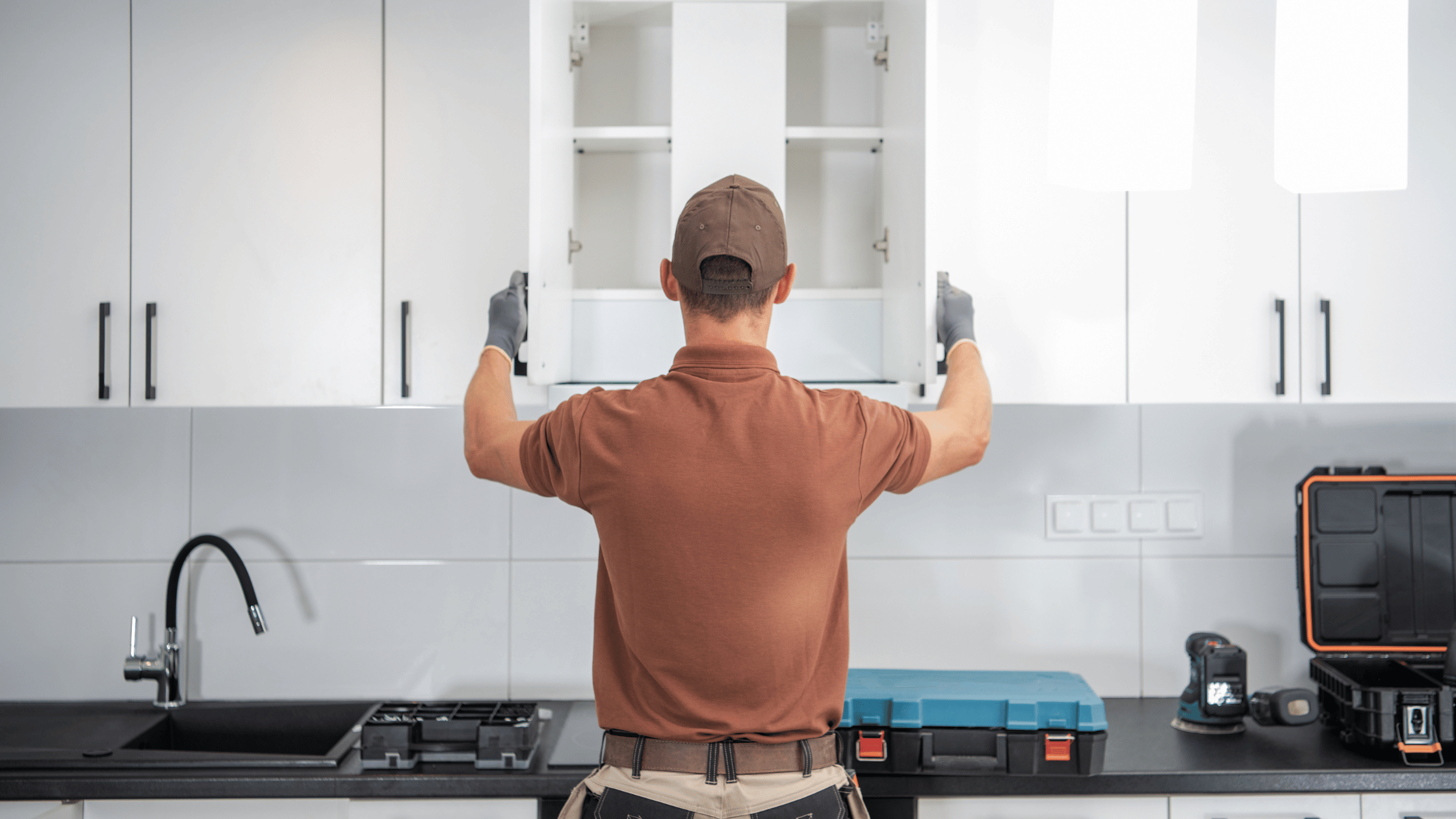 Worker installing a white kitchen cabinet with tools on the countertop.