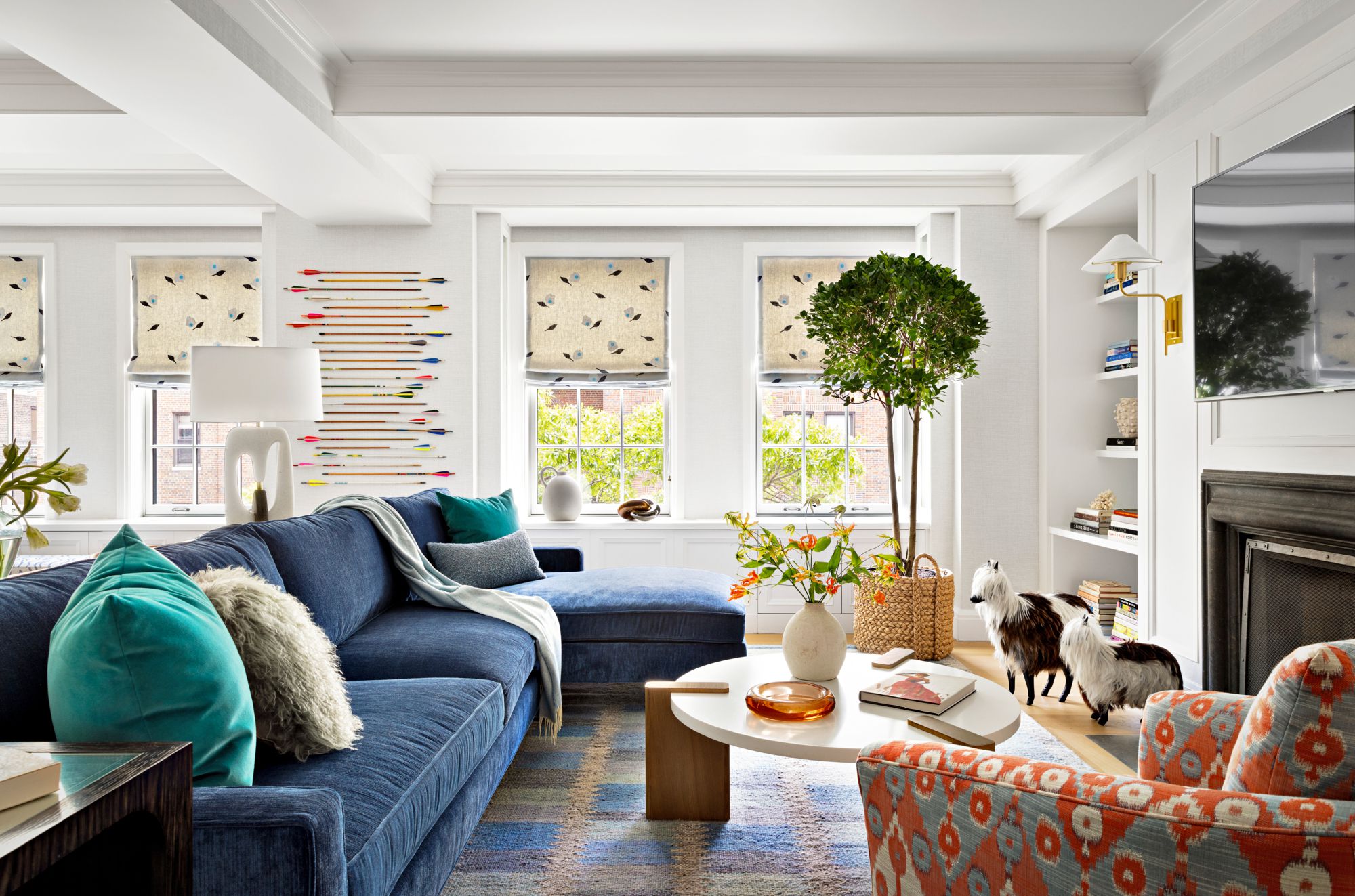 Colorful and eclectic living room with blue sectional sofa, patterned armchair, large windows, and playful decor.