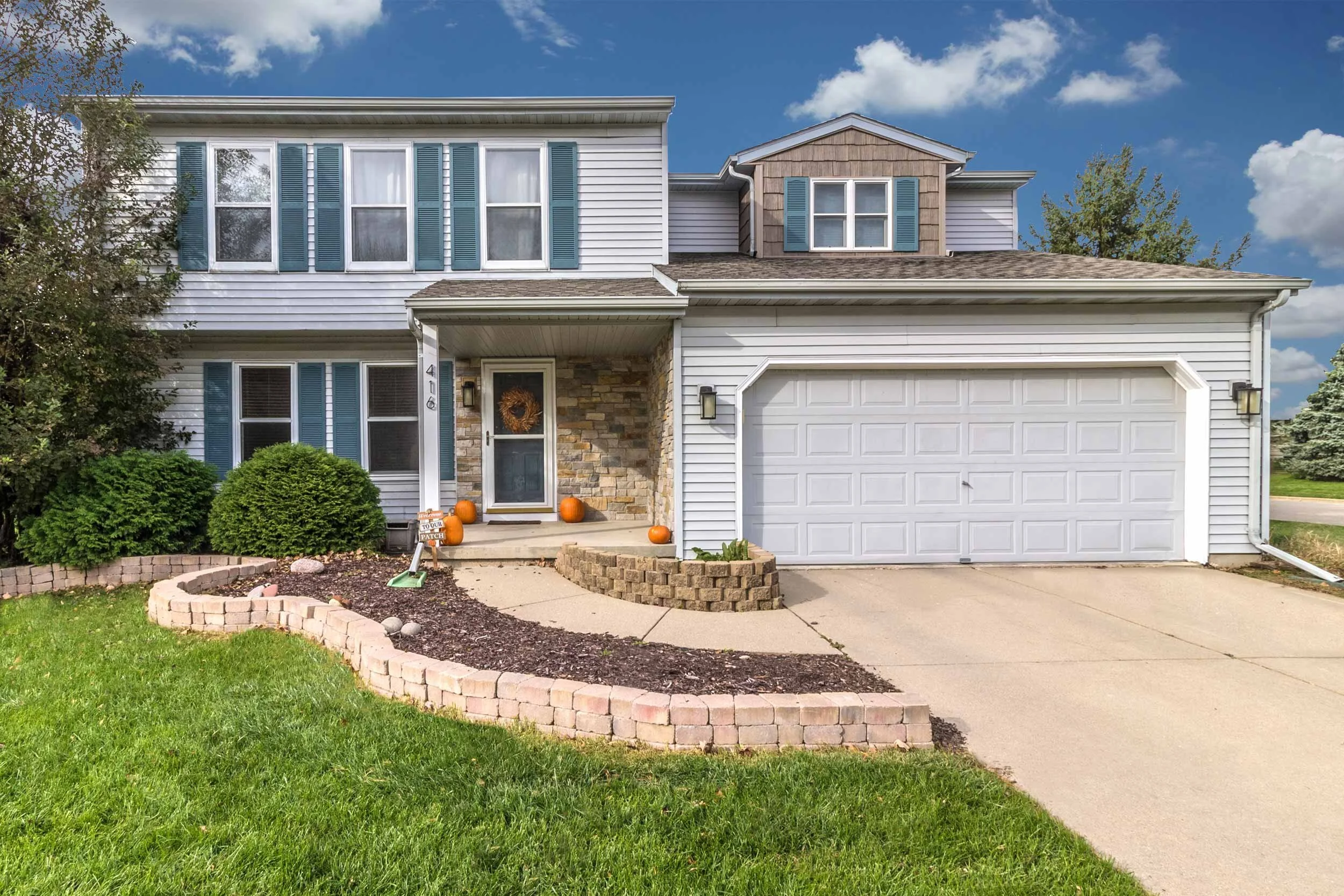 Two-story suburban home with blue shutters, stone accents, a front porch, and an attached garage.