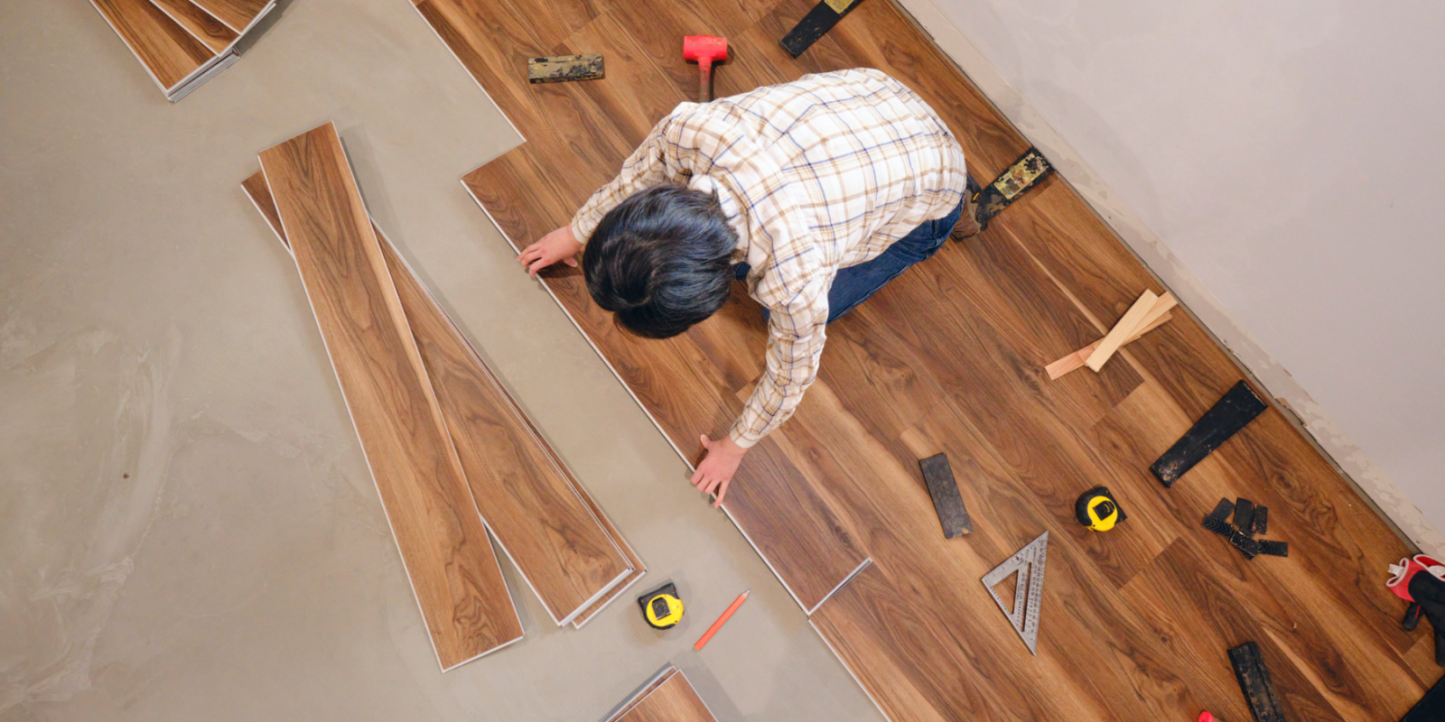 Person installing wood-look vinyl plank flooring using tools and measuring tape.