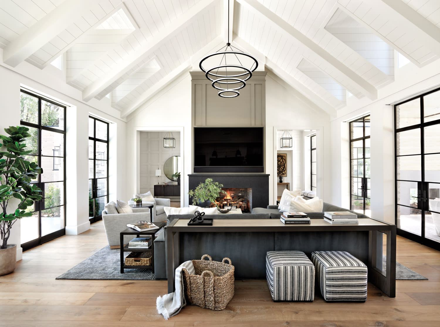 Modern living room with vaulted white ceiling, black-framed windows, and a sleek fireplace.