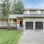 Two-story suburban home with green siding, black garage doors, and front porch.