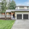 Two-story suburban home with green siding, black garage doors, and front porch.