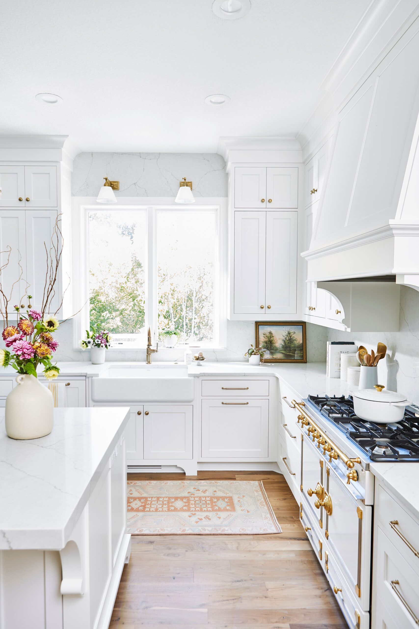 Bright white kitchen with gold hardware, farmhouse sink, marble countertops, and floral accents